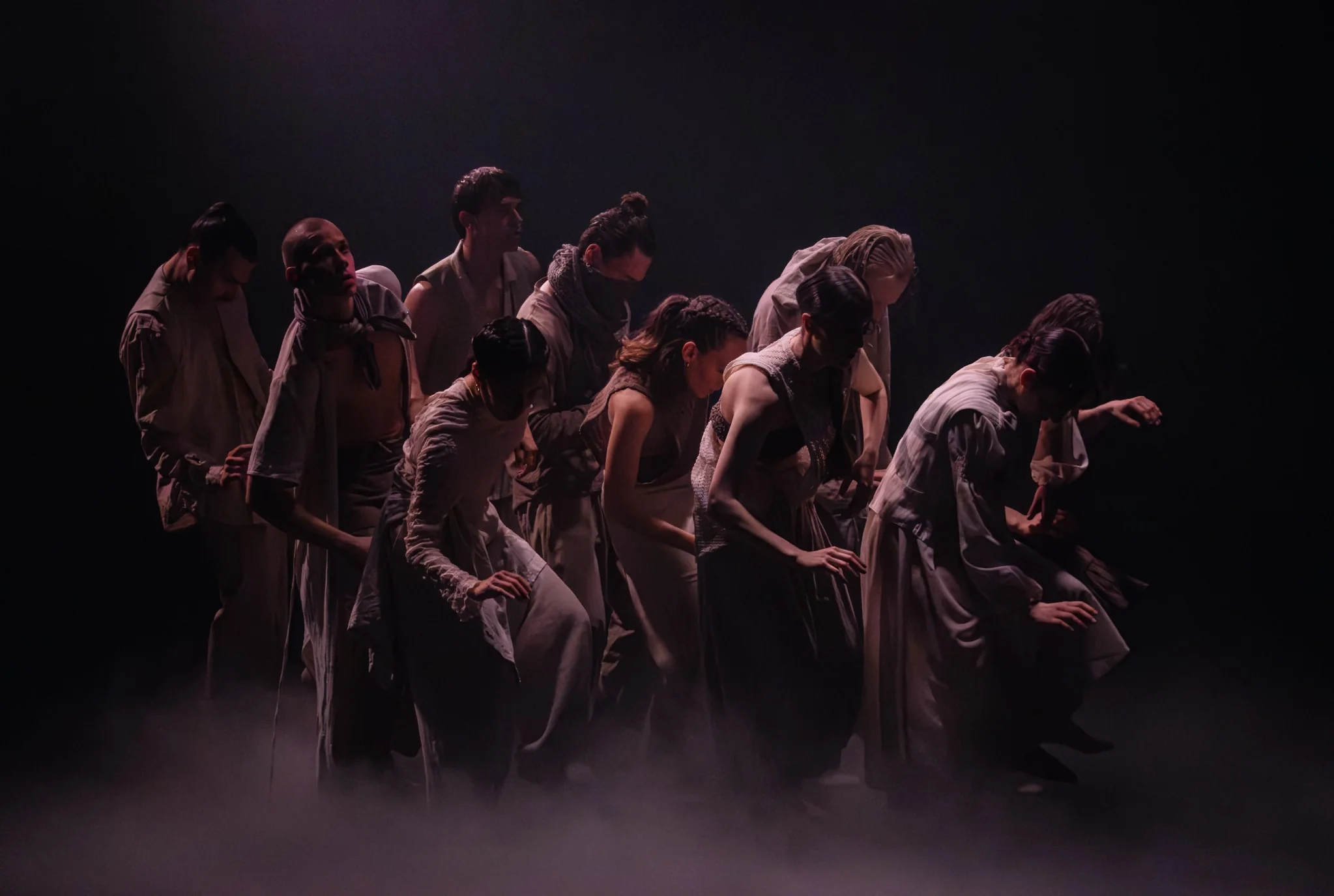 The Travelers ensemble moving together through a dark, hazy stage
